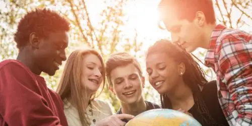 Students standing around a globe while looking at it and smiling