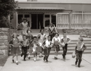 Group Of Grade School Children Running Down School Stairs With Books &amp; Bags